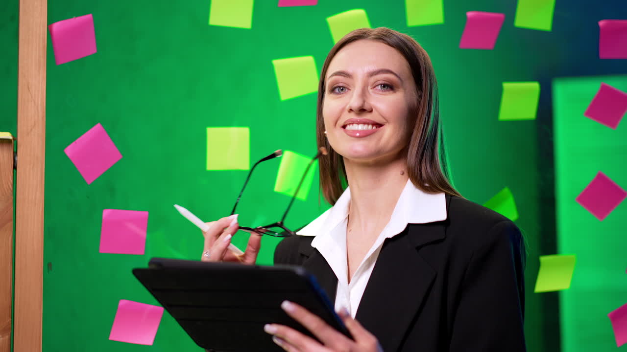Creative woman in brainstorming. A young woman in a black suit writes on a tablet surrounded by colorful sticky notes on a green background