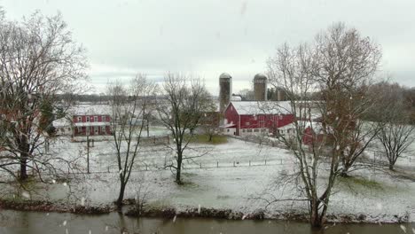 aerial establishing shot of family farm with red barn, brick house during winter snowstorm