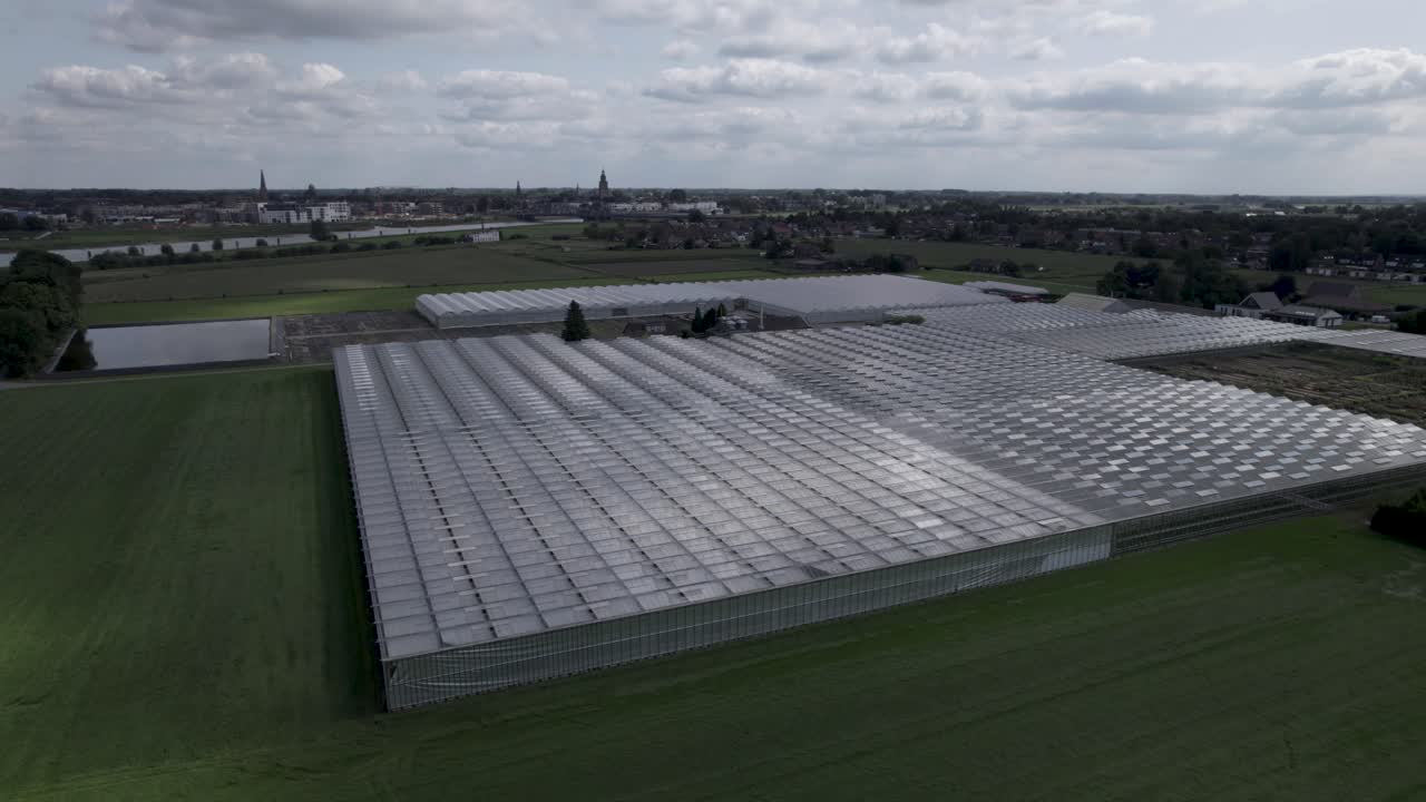antena constante de sombras proyectadas por las nubes que pasan sobre los invernaderos en el campo de la pradera con el paisaje urbano de zutphen en el fondo con el río ijssel en el medio y nubes cúmulos arriba