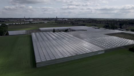 steady aerial of shadows cast by passing clouds over greenhouses in meadow field with countenance cityscape of zutphen in the background with river ijssel in between and cumulus clouds above