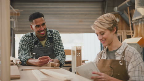 Männliche-Und-Weibliche-Auszubildende,-Die-Als-Tischler-In-Einer-Möbelwerkstatt-Arbeiten,-Messen-Holz-Und-Machen-Sich-Notizen