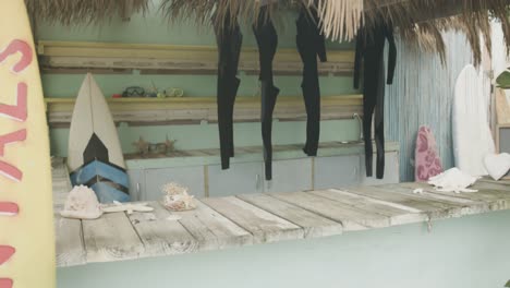 surfboards and hanging wetsuits in surf rental beach shack, slow motion