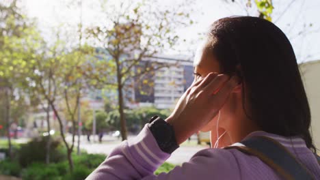 Side-view-of-asian-woman-wearing-earphones-standing-in-the-park