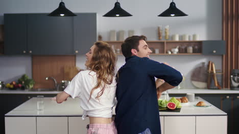 una pareja feliz bailando de espaldas a espaldas en la cocina de casa. amigos emocionados divirtiéndose.