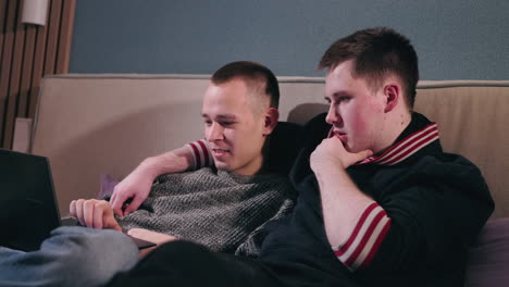 two men watching something on a laptop together on a couch