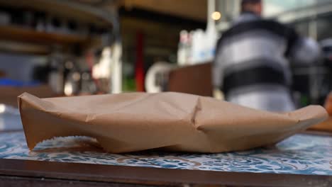 paper bag sits on a table waiting to be picked up, while a waiter makes coffee in background
