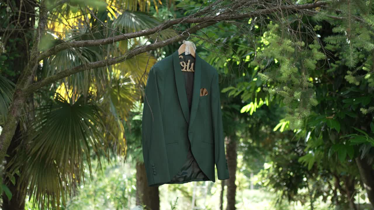 Groom's green wedding suit on a hanger, elegantly displayed on a tree branch