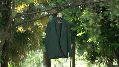 groom's green wedding suit on a hanger, elegantly displayed on a tree branch