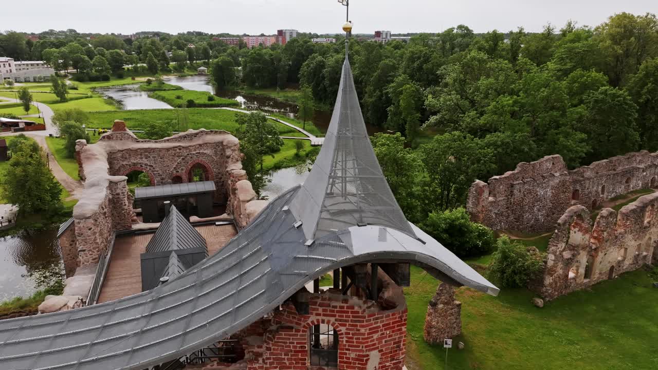 Drone performs cinematic orbit around restored castle tower in cloudy Dobele