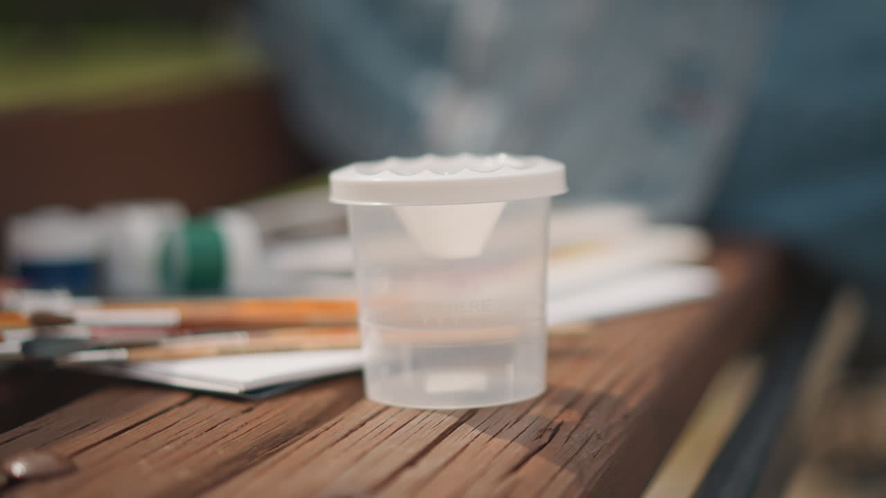 Ferramentas de pintura sob luz natural. Artista de aquarela serena arrumando pincéis e paleta na natureza. Vista em close-up da artista organizando habilmente ferramentas de pintura em um ambiente externo tranquilo.