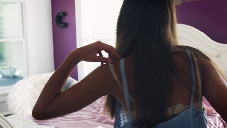 una adolescente entra en el dormitorio y se sienta en la cama para usar la computadora portátil