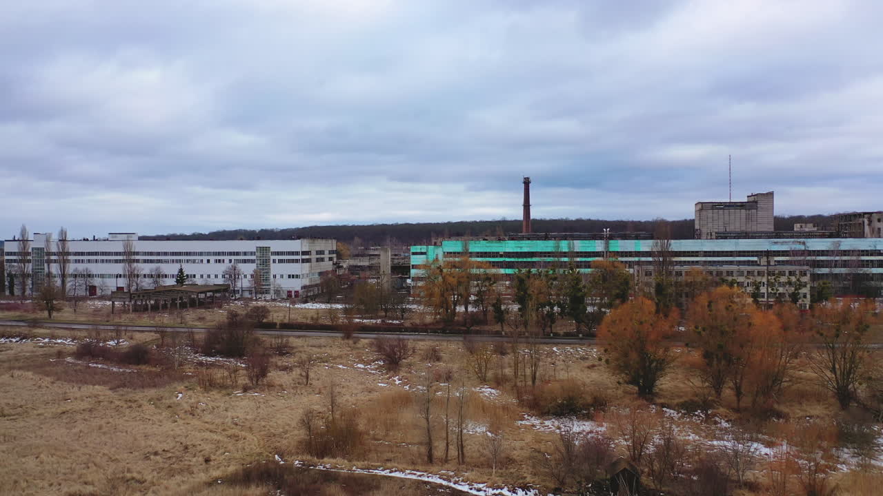 Old ruined factory among nature. Front view of a large ruined buildings of abandoned plant under gray sky.