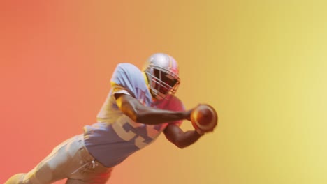 Video-of-african-american-american-football-player-catching-ball-over-yellow-to-orange-background