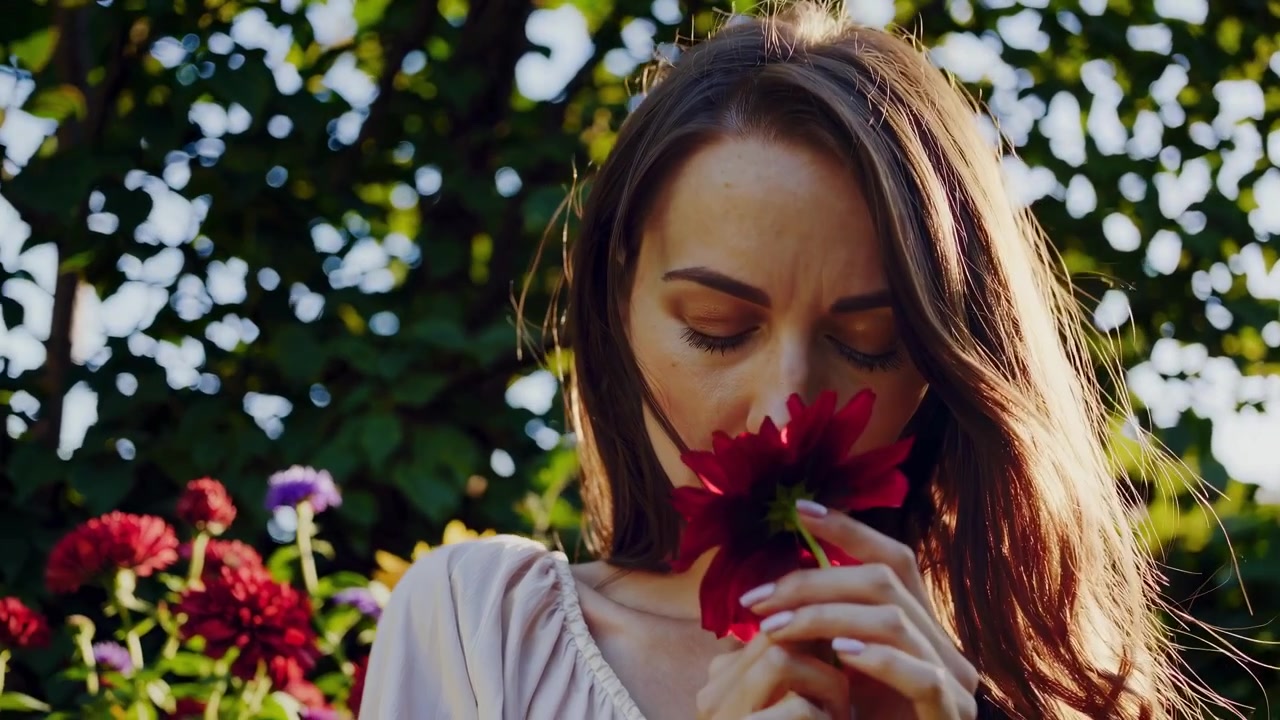 Ung kvinde, der dufter til en rød blomst i en have