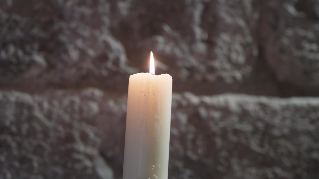 Fiamma di candela bianca che brilla davanti a un muro di pietra scuro e strutturato