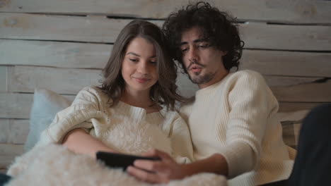 young cute couple in bed watching something funny on the phone