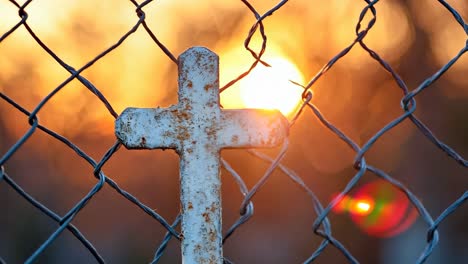 a rusty cross on a chain link fence with the sun setting behind it