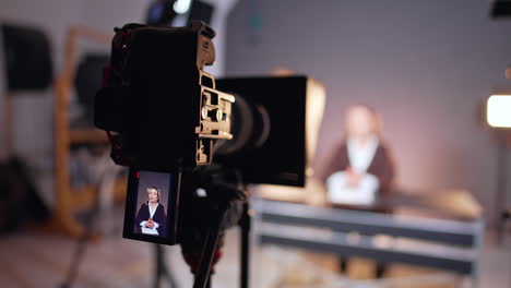 professional camera recording a female reporter sitting at desk at blurred backdrop. close up. blogging, tv program, newsreader concept.