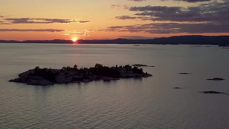 high view of rocky pine tree island in blue lake at sunset, drone aerial wide dolly in