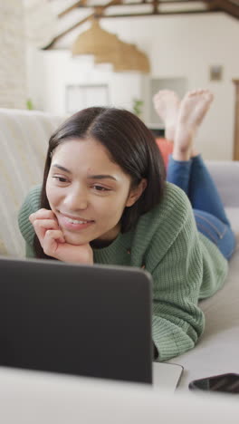 video vertical de una mujer biracial usando una computadora portátil y sonriendo