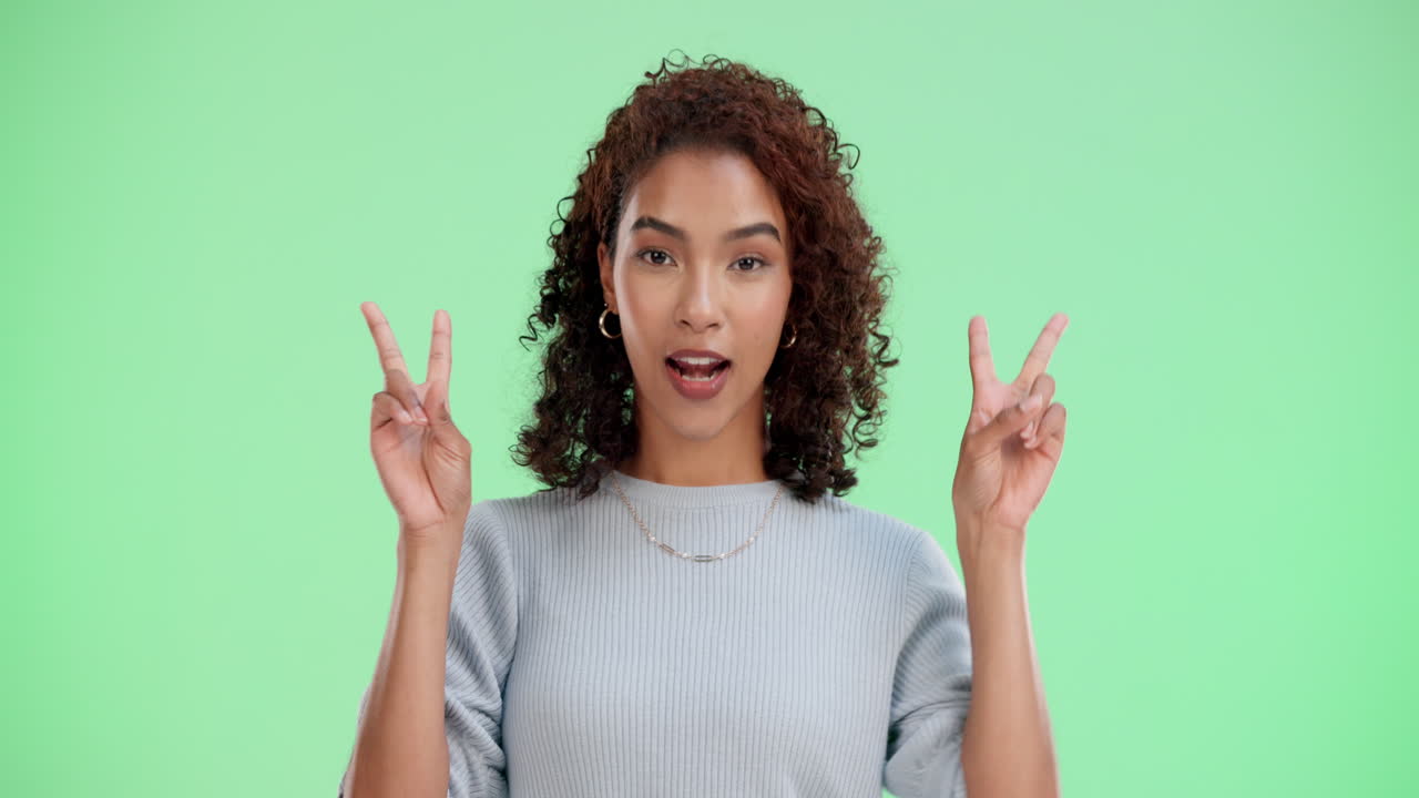 Woman making peace sign on light green background