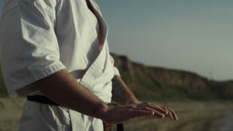 manos maestro de artes marciales haciendo calentamiento de pie en la playa al atardecer de cerca.