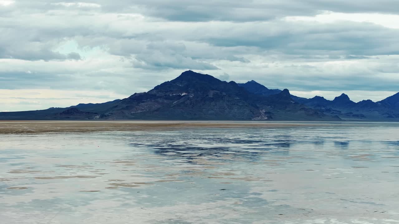 Wide Aerial drone trucking left shot of the Bonneville Salt Flats in Utah near Wendover Nevada flooded from rain creating mirage reflections with mountains in the background on a stormy spring evening