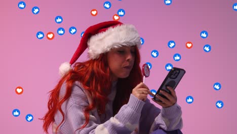 gen z mulher vestindo chapéu de papai noel comendo doce pirulito olhando para o telefone móvel com emojis de gráficos de movimento mostrando várias notificações de mídia social gostando e reagindo ao conteúdo on-line 1