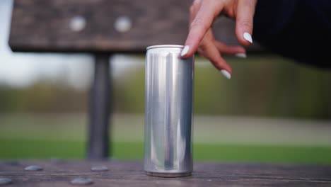 Female-hand-with-manicure-nails-touch-and-tap-on-shiny-aluminium-beverage-can