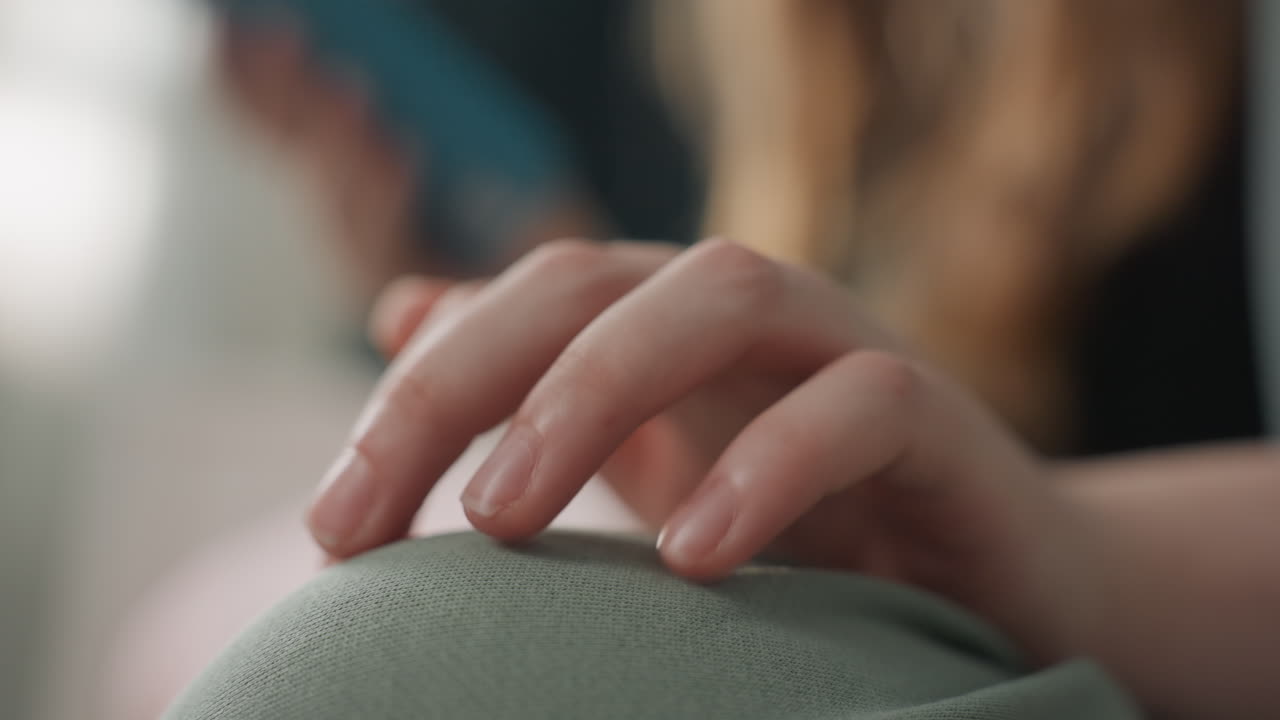 Closeup hand on green cushion with blurred figure, gentle tapping and light pressure, student gesture while scrolling phone, warm indoor light, emphasis on motion and textile texture