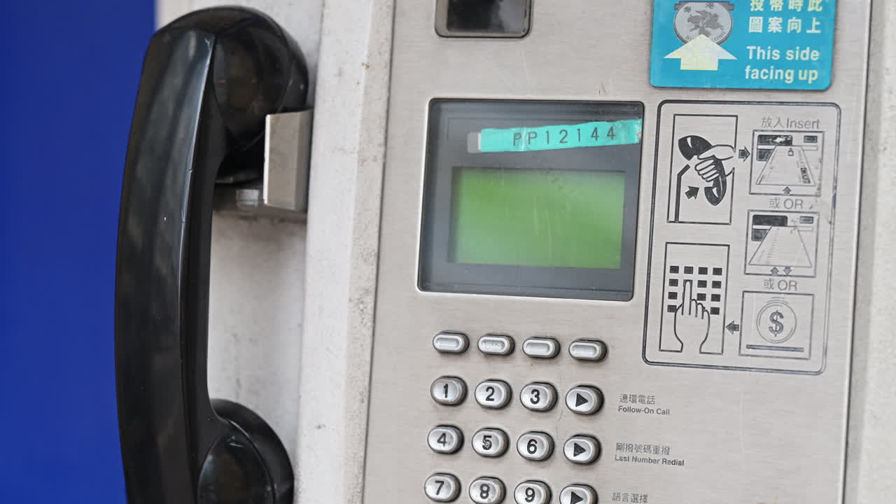 Close-up of a functional public payphone on a Hong Kong street. Shot illustrates the persistence of analog communication and essential emergency infrastructure in the smartphone era