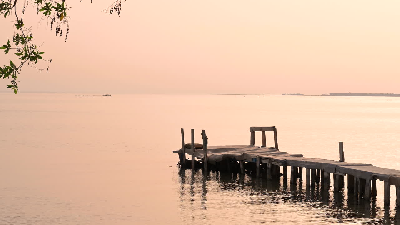 Beautiful wooden pier on the sea water waves with green leaves frame over sky, and small island background, Bahrain