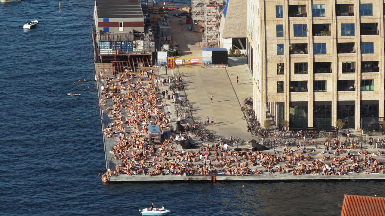 Aerial drone view of the busy Islands Brygge waterfront filled with swimmers, sunbathers, and cyclists