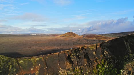 Lighthouse-On-A-Hill-Camera-Flying-Backwards-Revealing-Large-Rocky-Beach-Cliffs-And-Blue-Ocean-Coast