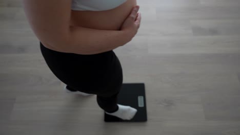 pregnant woman checking weight while gently touching belly at home, third trimester moment