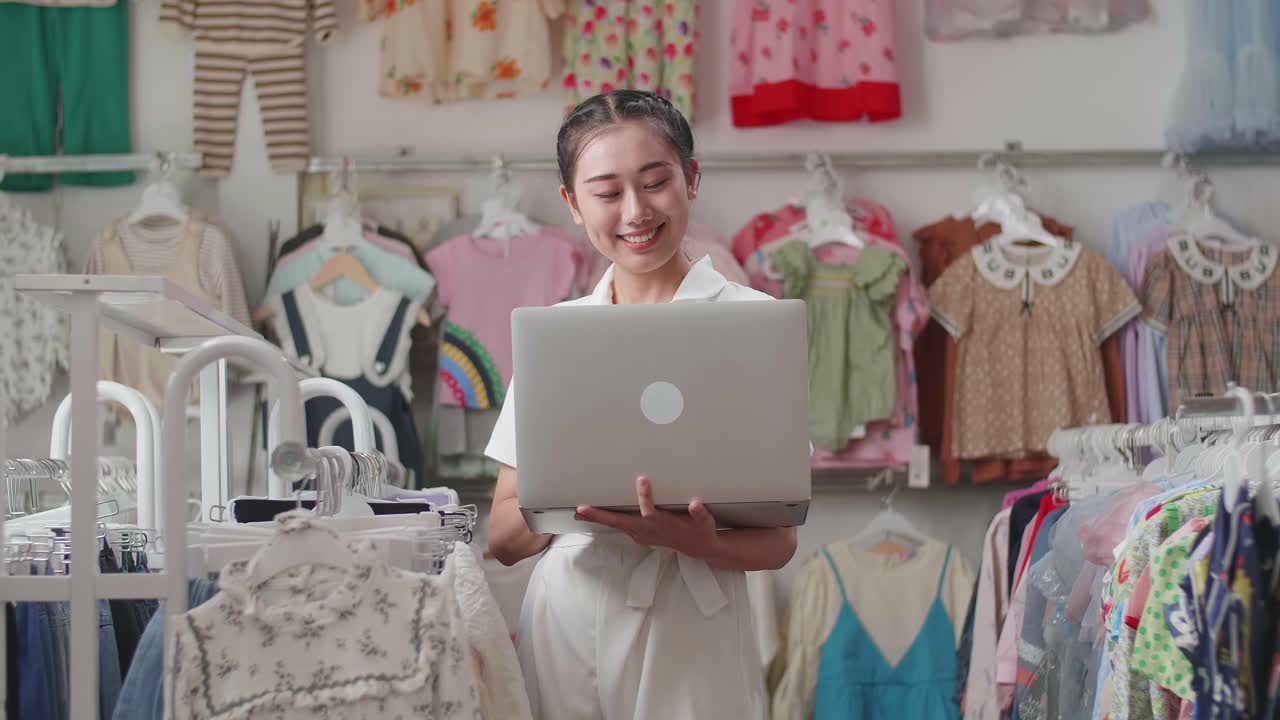 la dueña asiática de una tienda de ropa para niños disfruta usando una computadora portátil para comprobar las existencias en los rieles