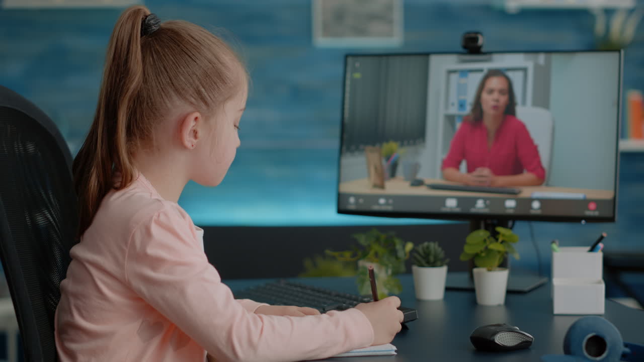 Pupil writing on textbook and talking to teacher on video call