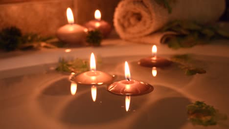 relajante fondo de spa con velas flotando en el agua del baño, algunos pétalos verdes y una toalla cerca de la superficie del agua