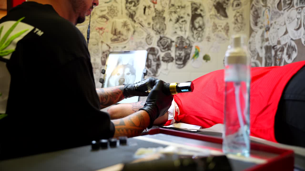 Zoom in shot of a tattoo artist creating intricate design on client's arm in studio with art-filled walls in background