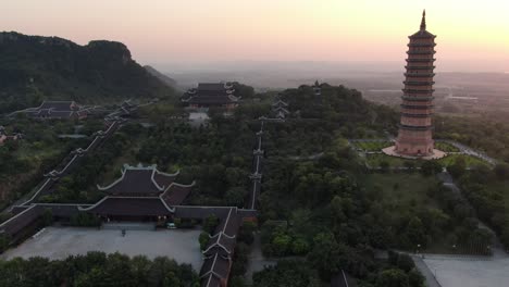 Drohnen-Luftaufnahme-In-Vietnam,-Die-Bei-Sonnenuntergang-über-Buddhistische-Tempelanlagen-Mit-Pagoden-Und-Mit-Grünen-Bäumen-Bedeckten-Straßen-In-Ninh-Binh-Fliegt