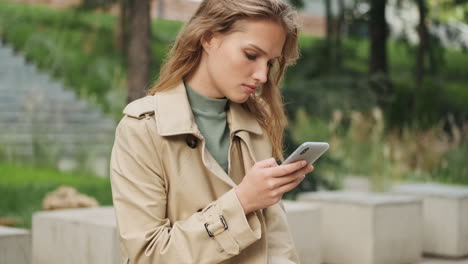 caucasian female student using smartphone outdoors.