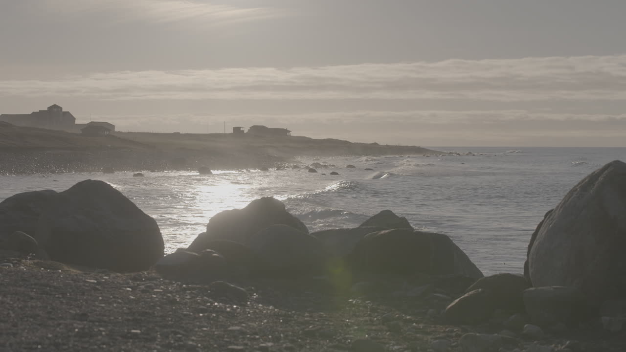 Big waves crashing on the beach near Reve Havn Borestranda Norway during sunset with the beach and sea in the background and the sun reflection in the water with rocks in the foreground LOG