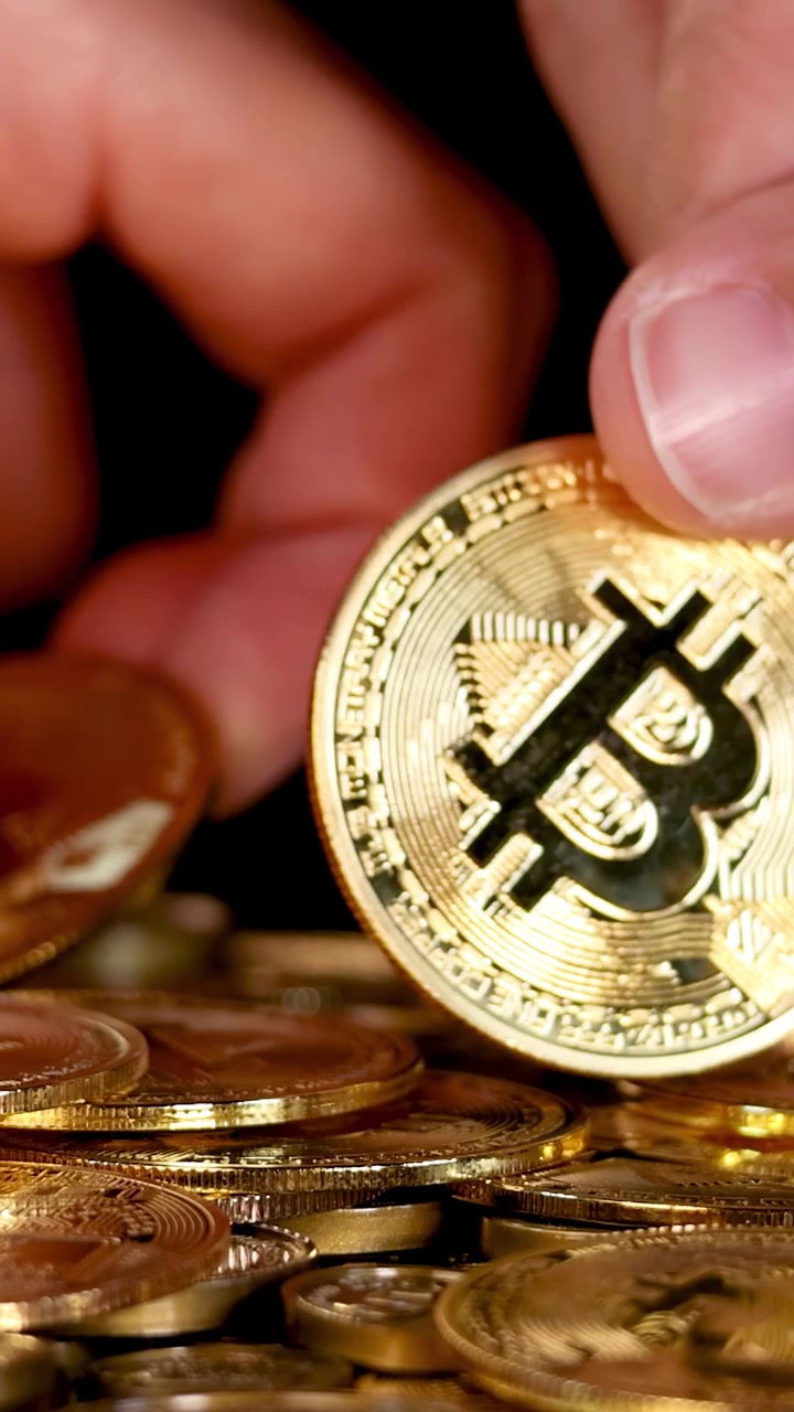 Mão humana seleciona e levanta moeda de criptomoeda dourada e brilhante de uma pilha, com iluminação de estúdio dramática