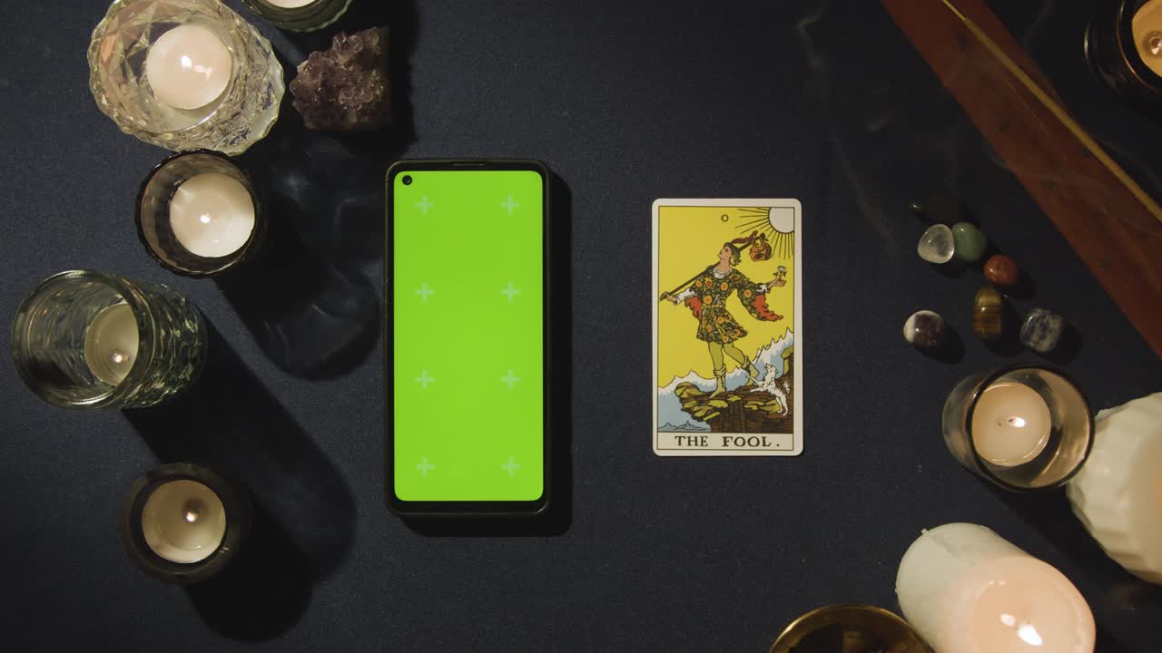 disparo aéreo de una persona que da lectura de tarot con pantalla verde teléfono móvil al lado de la tarjeta de tonto en la mesa