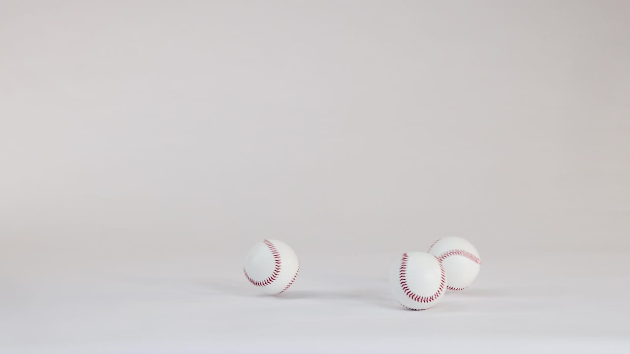 Diverse palle da baseball bianche con cuciture rosse rimbalzano e rotolano su un pavimento pulito di uno studio bianco
