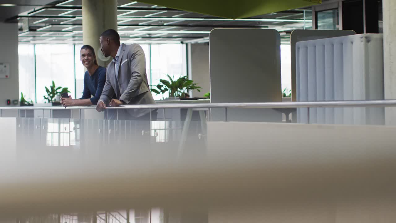 Diverse businessman and businesswoman talking in corridor of modern office