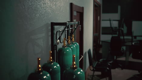 tanks of compressed gas line a wall in a dimly lit industrial setting