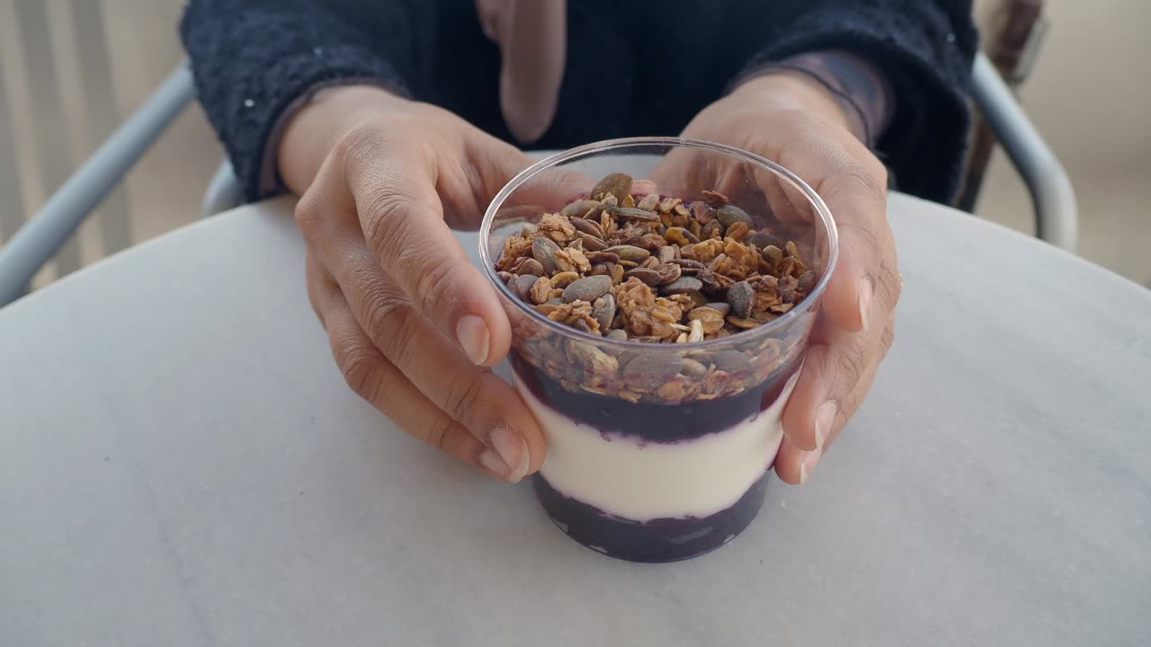 Mani che tengono un parfait di yogurt salutare con granola e frutta