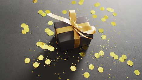 black gift box with gold ribbon with gold glitter on black background