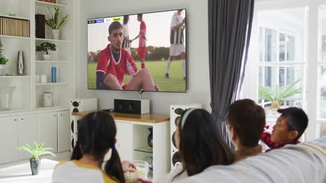 Asian-family-watching-tv-with-diverse-male-soccer-players-playing-match-on-screen